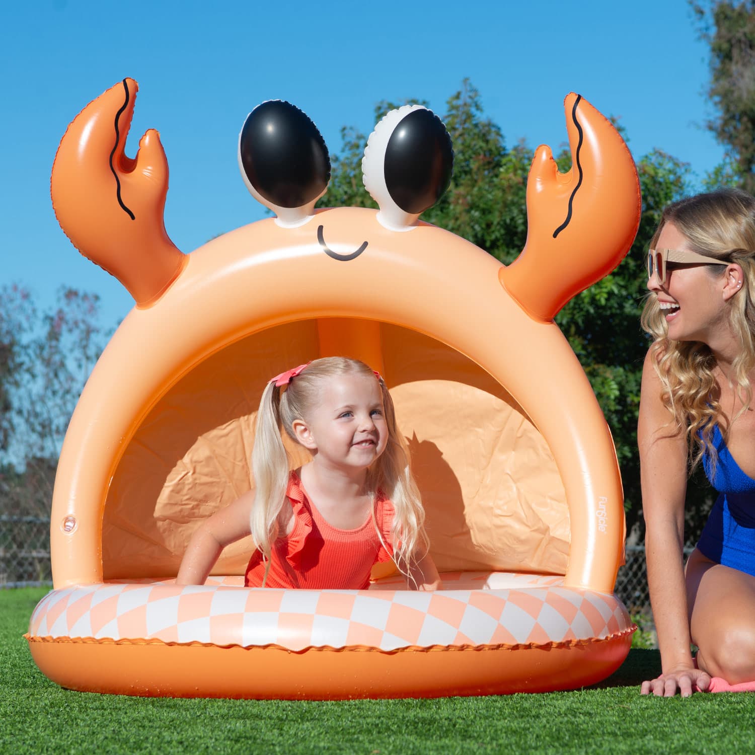 Inflatable crab-shaped pool with a child and adult in a grassy area.