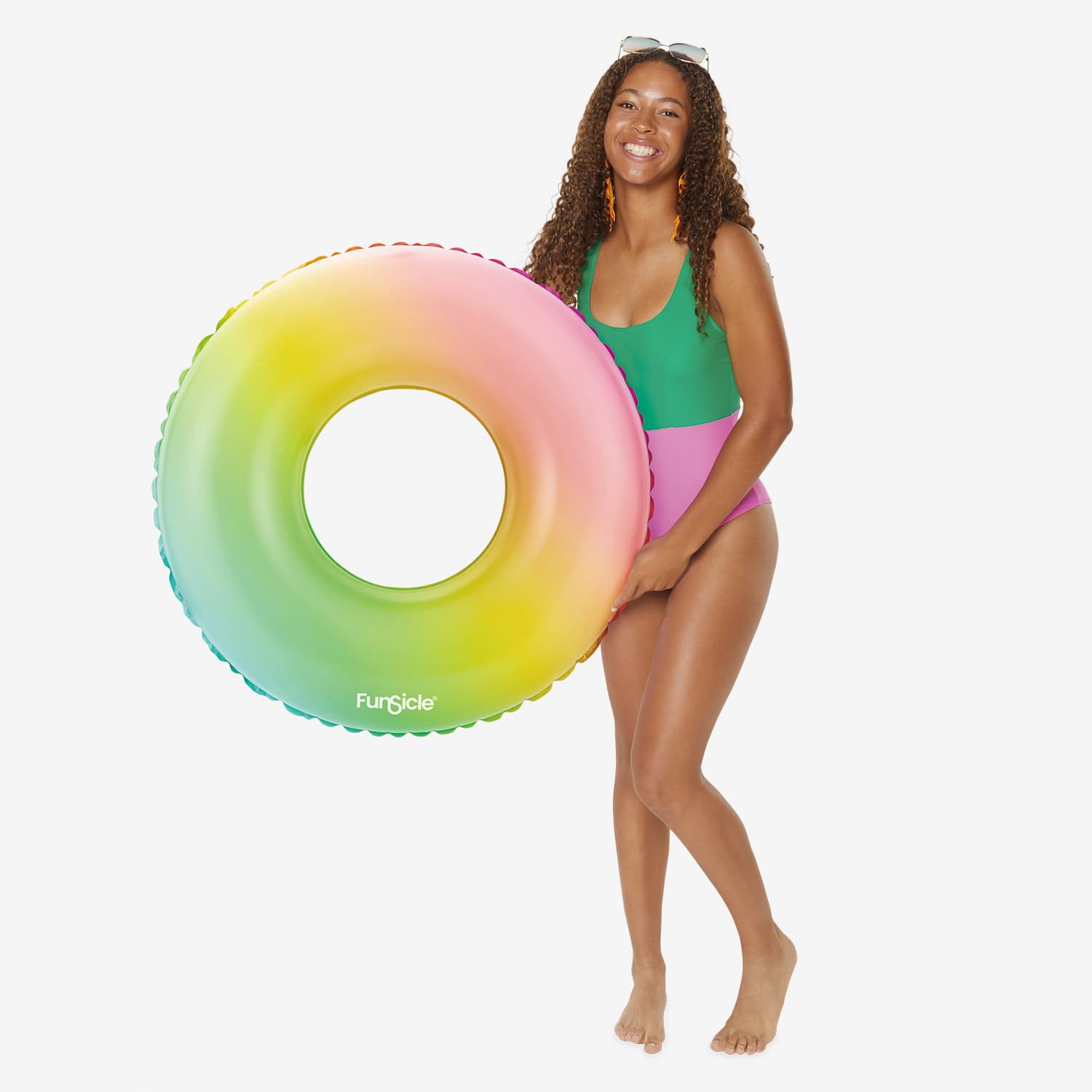 Woman in a green and pink swimsuit holding a colorful inflatable ring on a white background