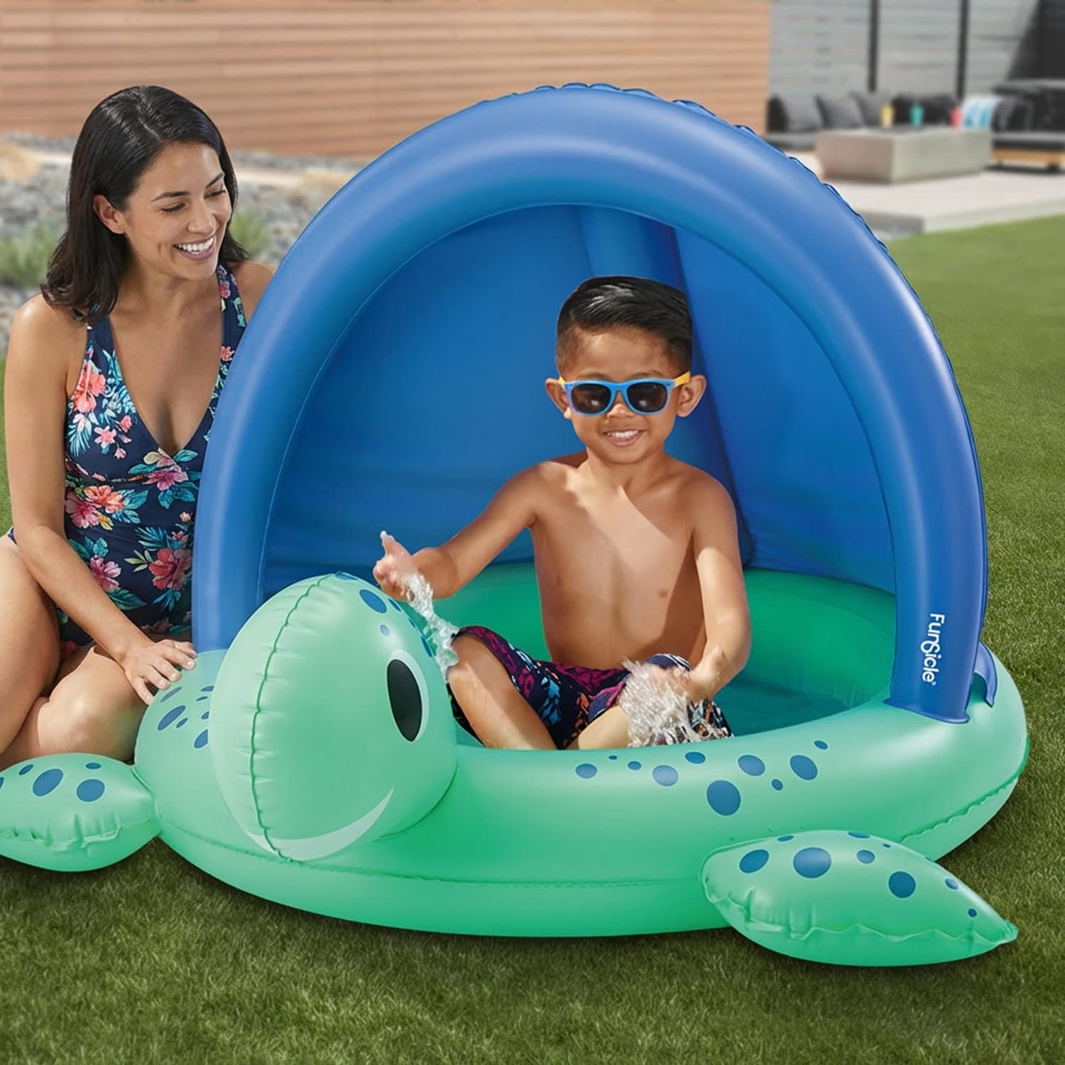 Child playing in a turtle-shaped inflatable pool with a canopy, supervised by an adult.