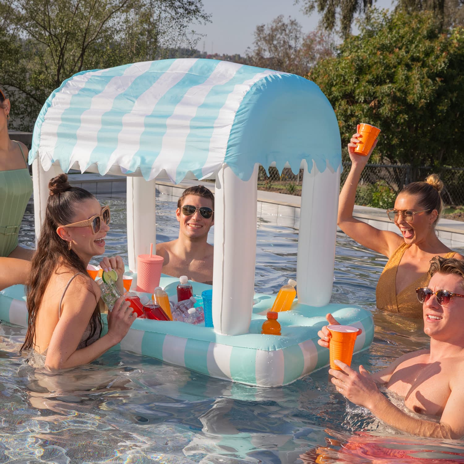 People enjoying a pool party with an inflatable striped cabana and drinks.